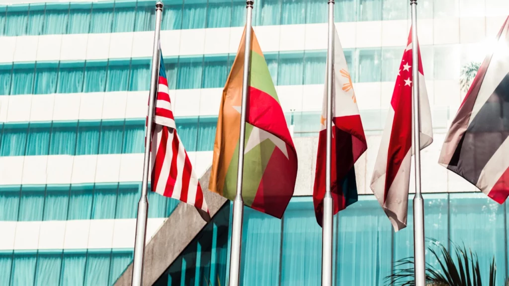 Diverse Länderflaggen wehen an einem Mast vor einer gläsernen Gebäudefassade