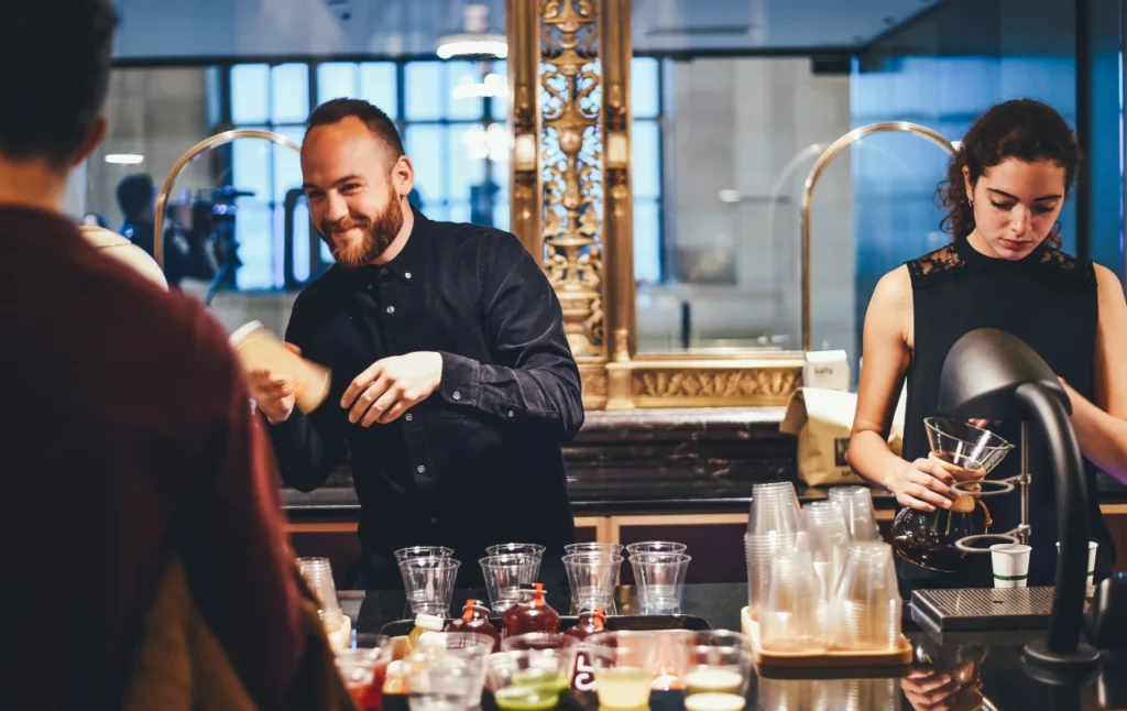 Ein Barmann und eine Barfrau bedienen Gäste und spülen Gläser